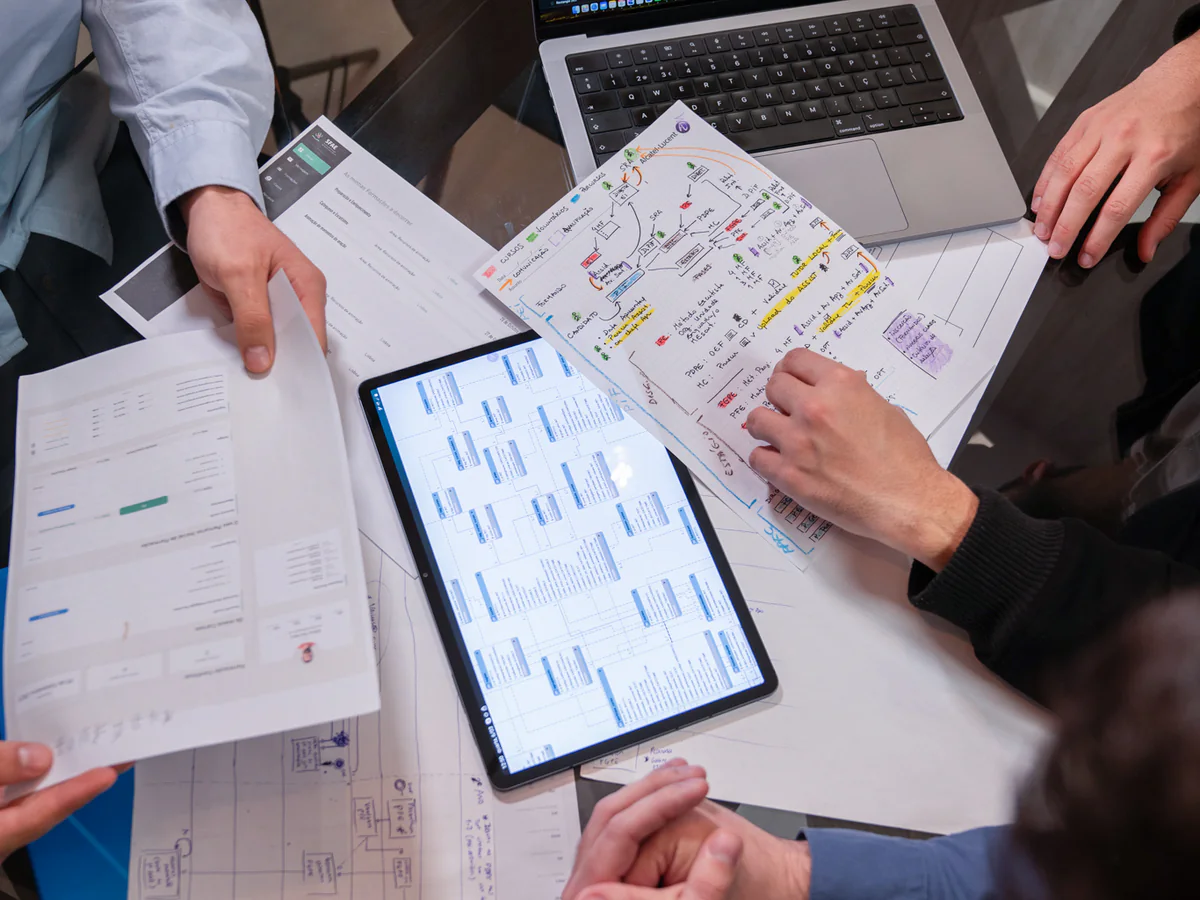 A meeting table from above, with a tablet, printed screens and annotated plans